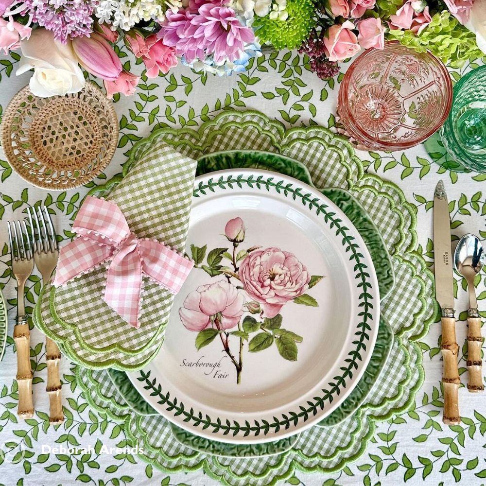 Table setting with floral plates, checkered napkins, and decorative cutlery on a patterned tablecloth.