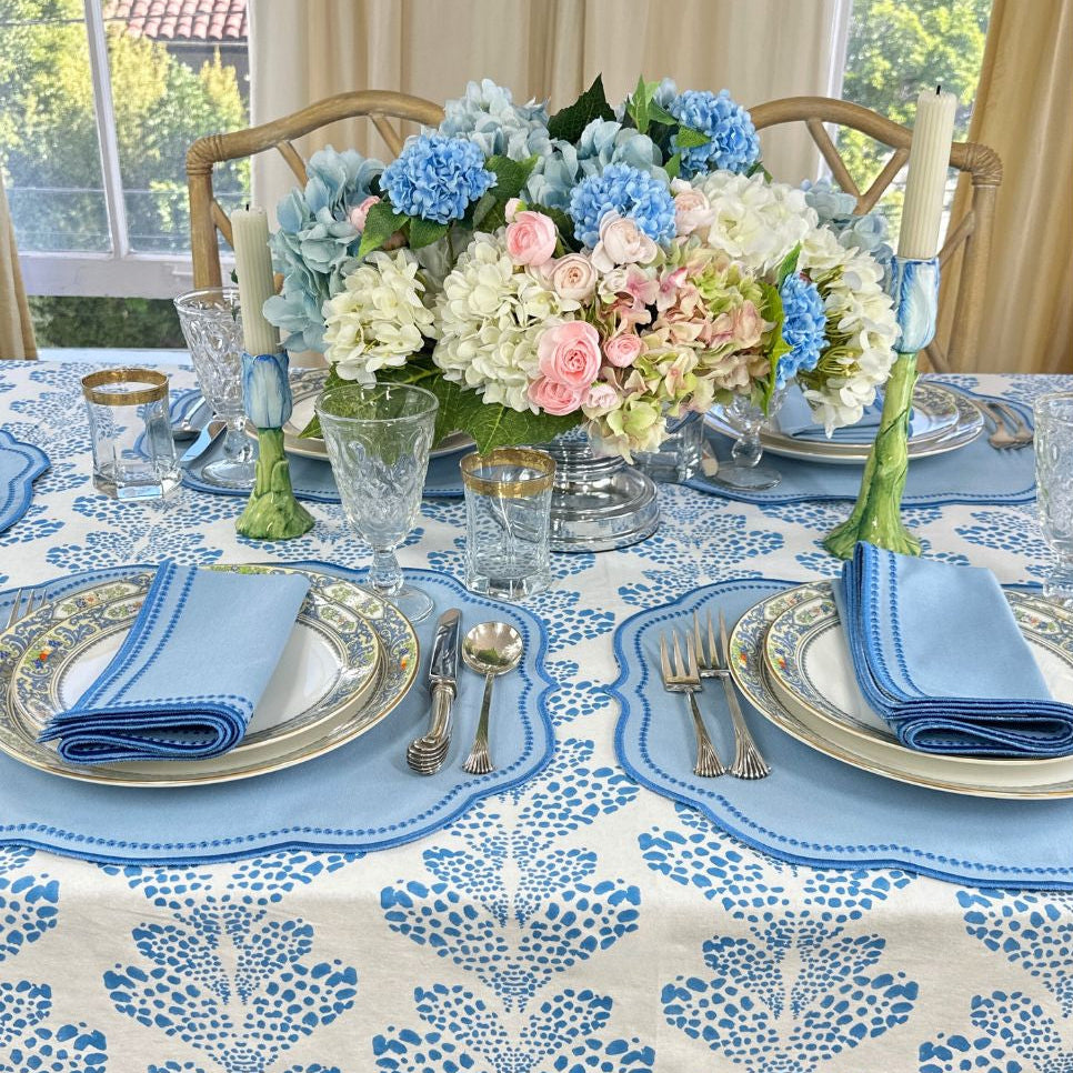 Elegant table setting with floral centerpiece, blue and white patterned tablecloth, and folded napkins.