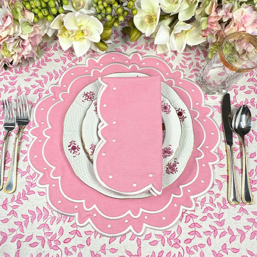 Table setting with pink placemat, white plates, and silverware on a floral tablecloth.