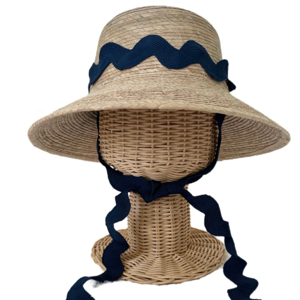 Woven sun hat with navy blue ribbon on a mannequin head against a white background