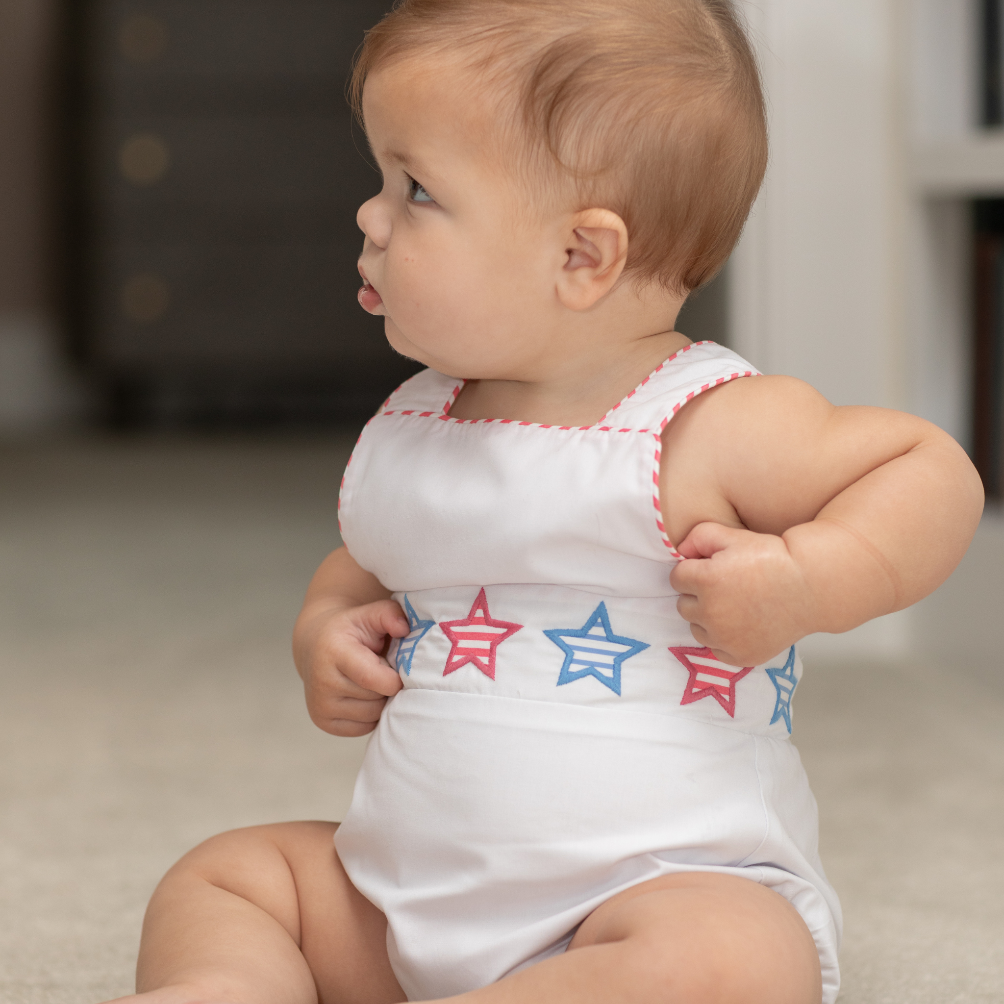 Henry Duvall unisex baby sunsuit in white with red and blue star appliqué and criss cross straps, classic patriotic outfit for Memorial Day, 4th of July, and summer occasions