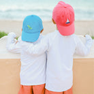 Two children wearing colorful caps and matching outfits standing back-to-back against a wall.