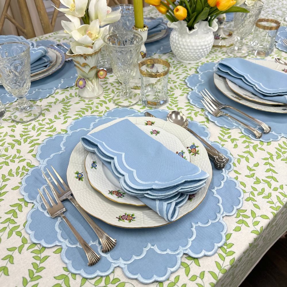 Elegant table setting with blue napkins, floral plates, and decorative glasses on a patterned tablecloth.