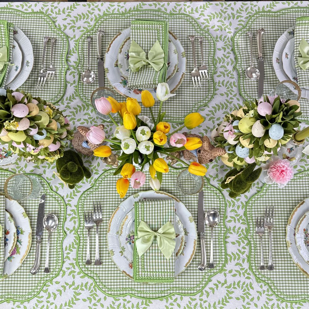 Easter-themed table setting with floral centerpieces, green checkered tablecloth, and decorative plates.