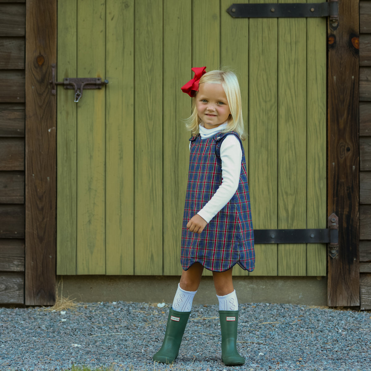 Henry Duvall Janie Jumper girls’ holiday dress in Tinsel Tartan, a navy, red and green plaid with subtle gold metallic thread, scalloped hem, navy piping and gold shoulder buttons.