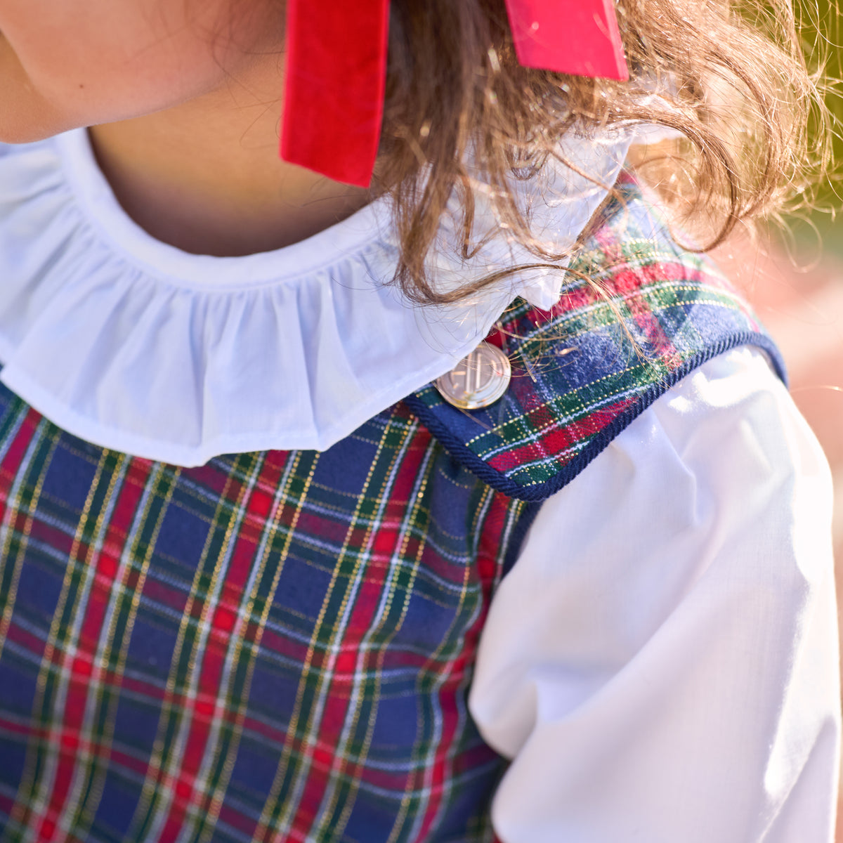 Henry Duvall Janie Jumper girls’ holiday dress in Tinsel Tartan, a navy, red and green plaid with subtle gold metallic thread, scalloped hem, navy piping and gold shoulder buttons.