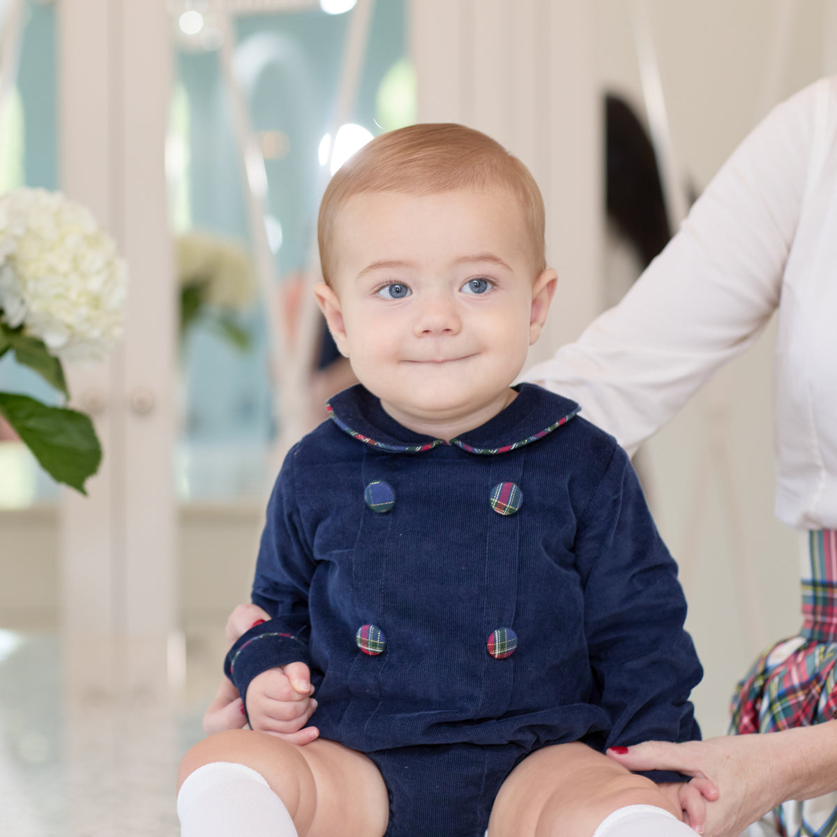Baby boys’ Banks Bubble in Midnight Blue Corduroy with Tinsel Tartan-covered buttons and coordinating plaid trim at the Peter Pan collar and cuffs.