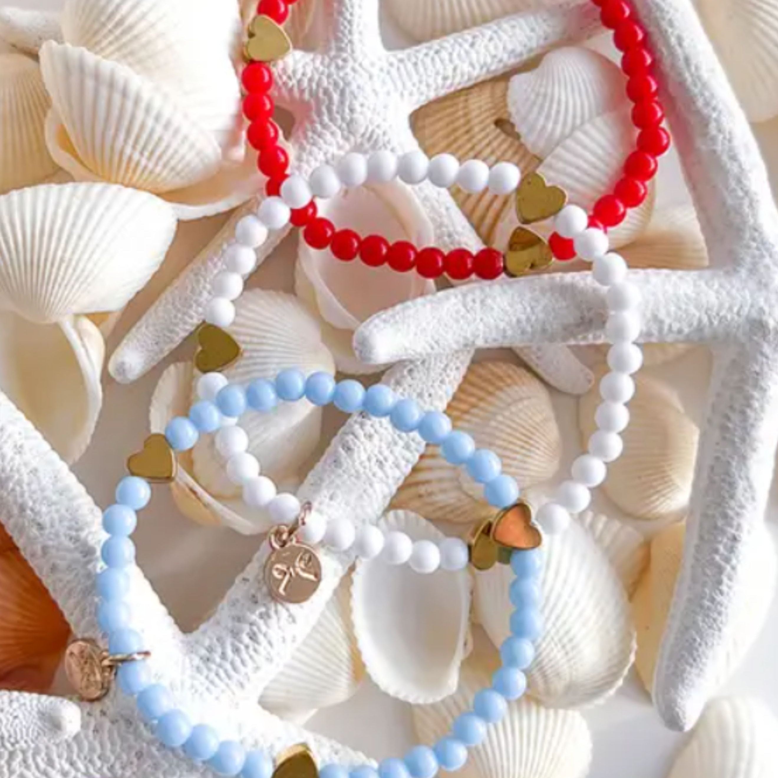Two beaded bracelets, one red and one blue, on starfish and shells.
