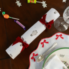 Decorative Christmas cracker on a table with a plate, spoon, and festive items.