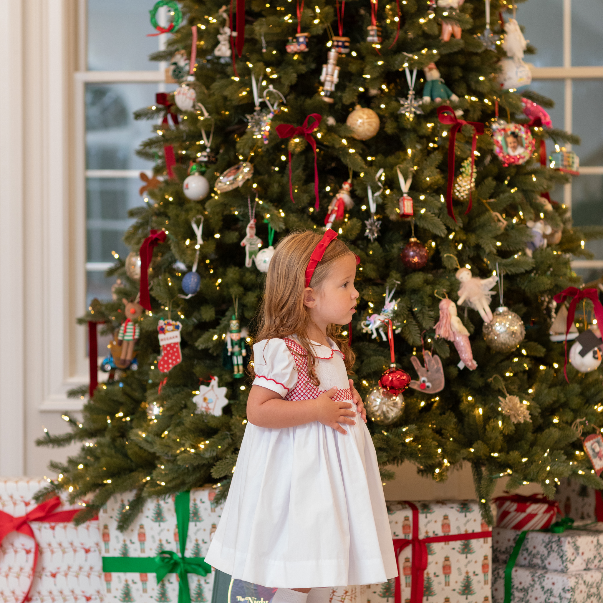 White short sleeve girls' holiday dress with red bow smocking across the chest, Peter Pan collar, and piped cuffs, classic Henry Duvall Eloise Dress for Christmas and winter family gatherings