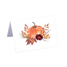 Watercolor Thanksgiving place card featuring a pumpkin illustration, displayed in a pale green pumpkin holder on a patterned fall tablecloth.