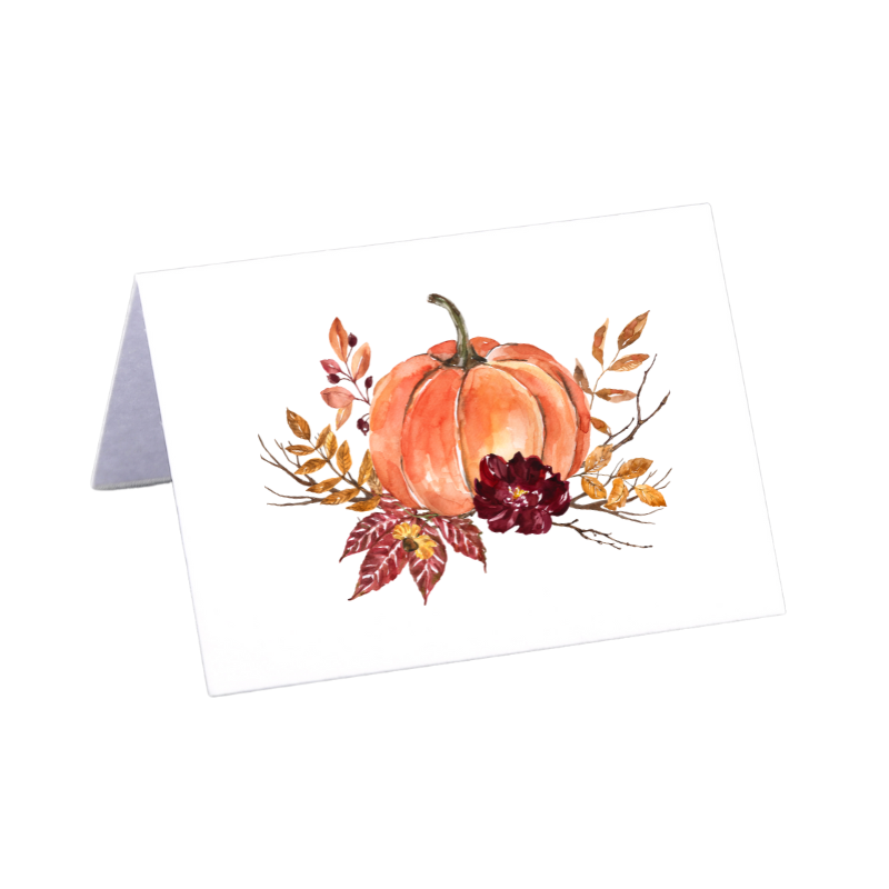 Watercolor Thanksgiving place card featuring a pumpkin illustration, displayed in a pale green pumpkin holder on a patterned fall tablecloth.