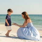 Woman walking along the beach wearing the Henry Duvall Kate Dress, a breezy striped women’s dress with coastal style.