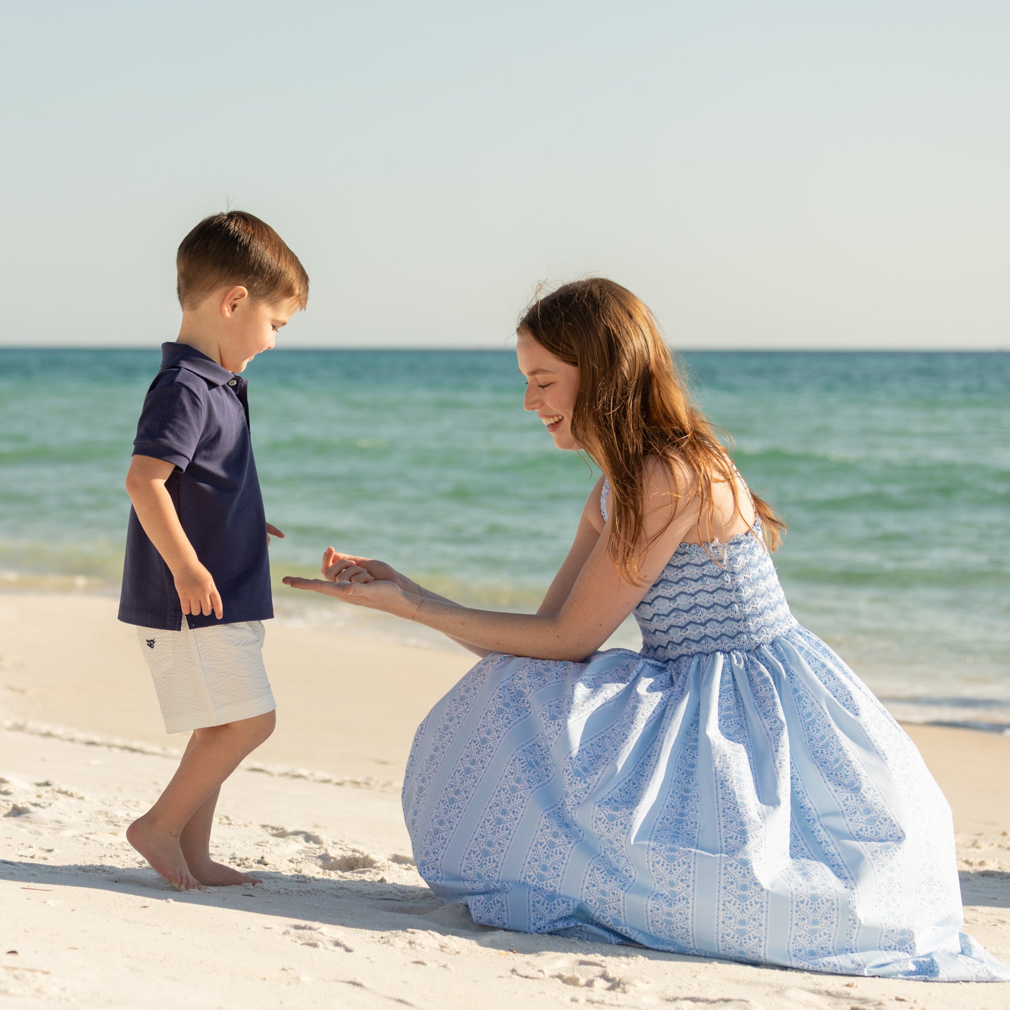 Woman walking along the beach wearing the Henry Duvall Kate Dress, a breezy striped women’s dress with coastal style.