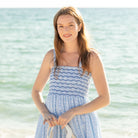 Woman walking along the beach wearing the Henry Duvall Kate Dress, a breezy striped women’s dress with coastal style.