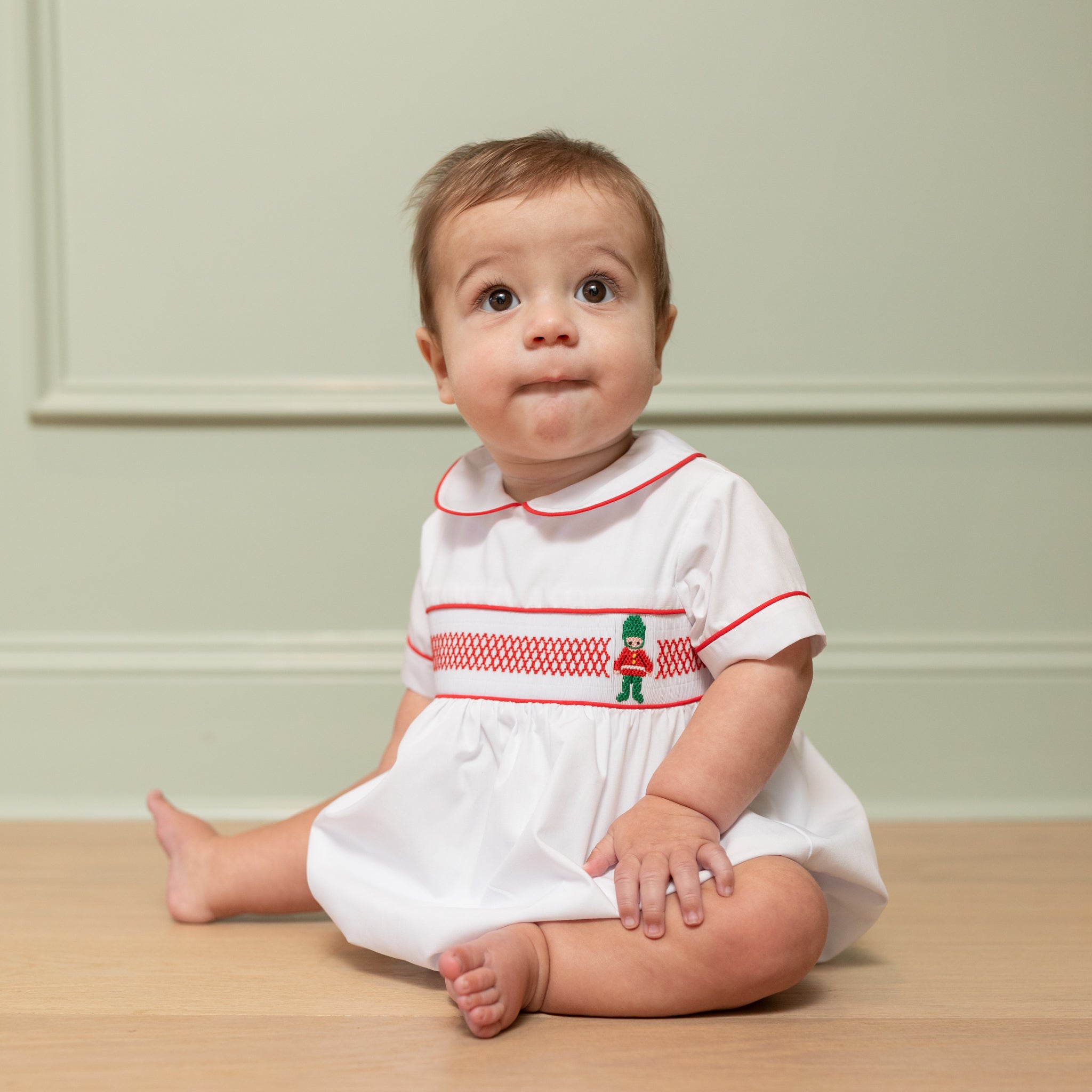 White baby boy holiday bubble with red toy soldier smocking and Peter Pan collar, Henry Duvall's Charlie Bubble in cotton poplin for Christmas celebrations