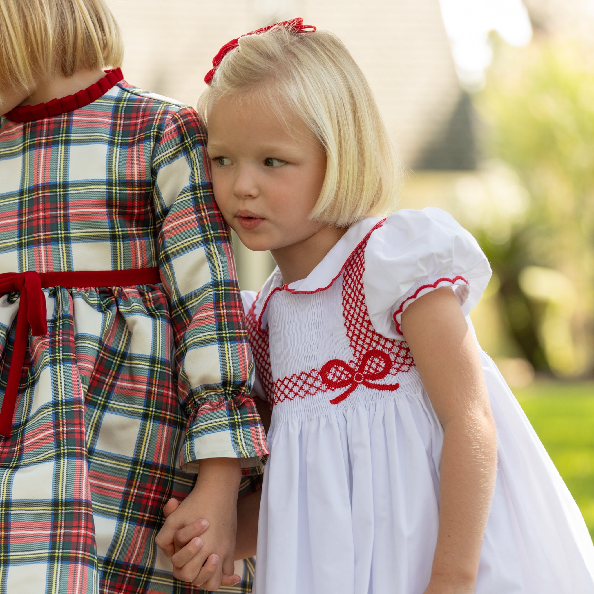 White short sleeve girls' holiday dress with red bow smocking across the chest, Peter Pan collar, and piped cuffs, classic Henry Duvall Eloise Dress for Christmas and winter family gatherings