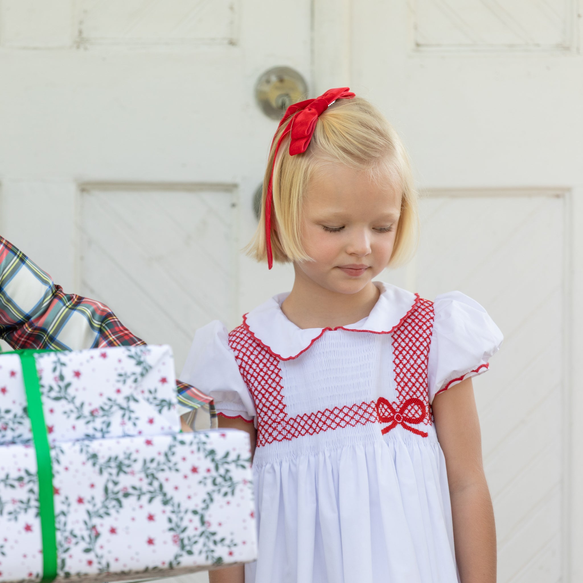 White short sleeve girls' holiday dress with red bow smocking across the chest, Peter Pan collar, and piped cuffs, classic Henry Duvall Eloise Dress for Christmas and winter family gatherings