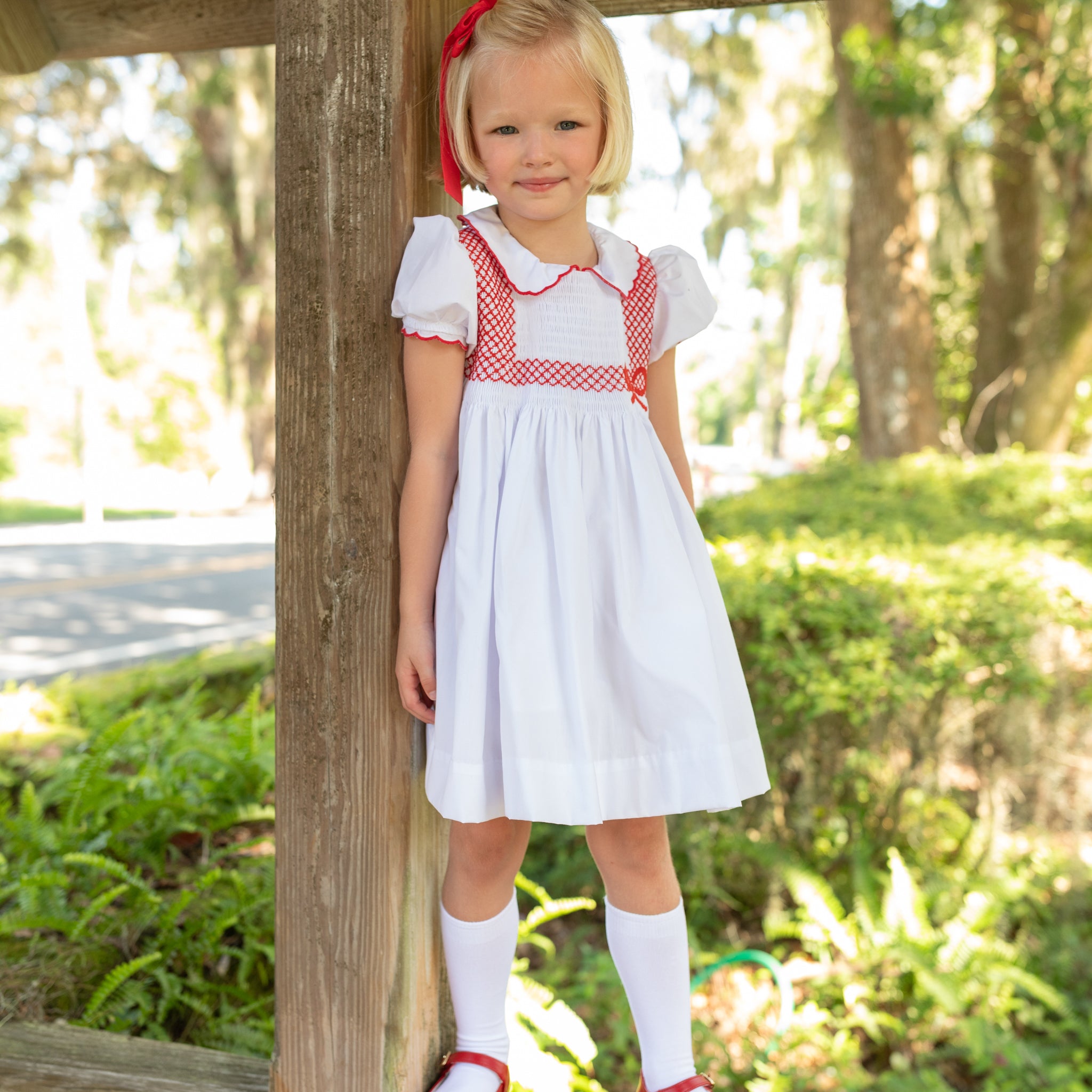 White short sleeve girls' holiday dress with red bow smocking across the chest, Peter Pan collar, and piped cuffs, classic Henry Duvall Eloise Dress for Christmas and winter family gatherings