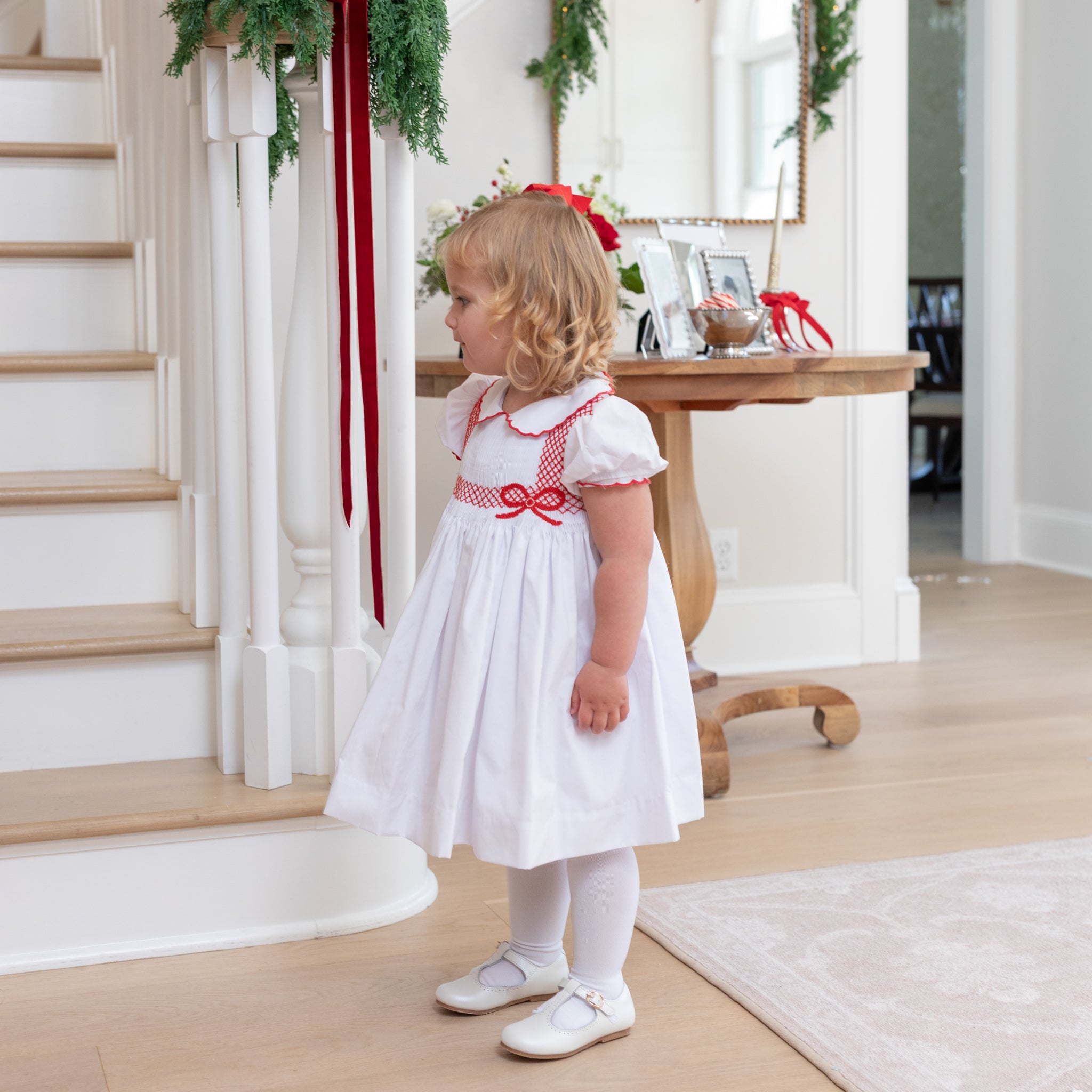 White short sleeve girls' holiday dress with red bow smocking across the chest, Peter Pan collar, and piped cuffs, classic Henry Duvall Eloise Dress for Christmas and winter family gatherings