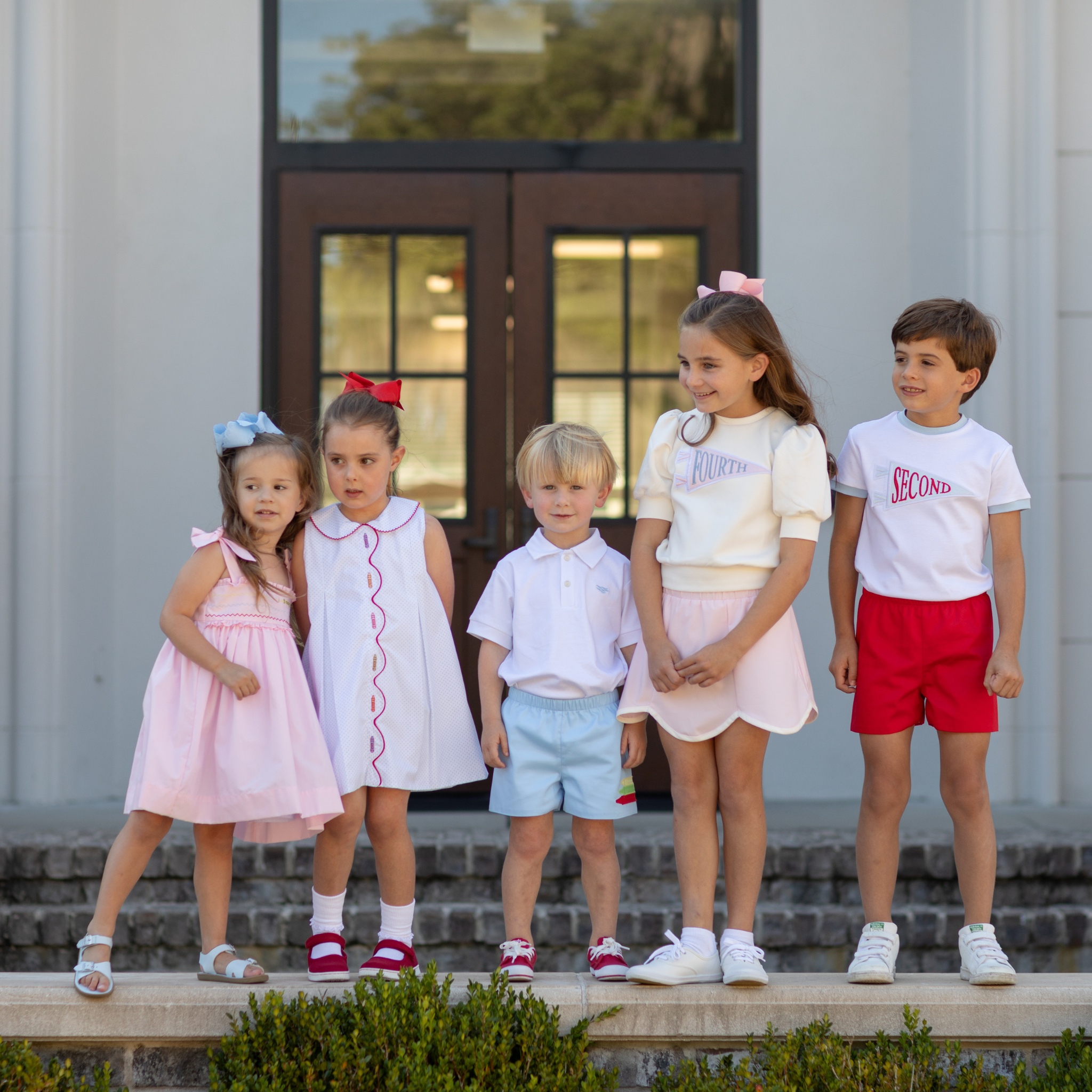 Five children in colorful outfits standing on steps outdoors.