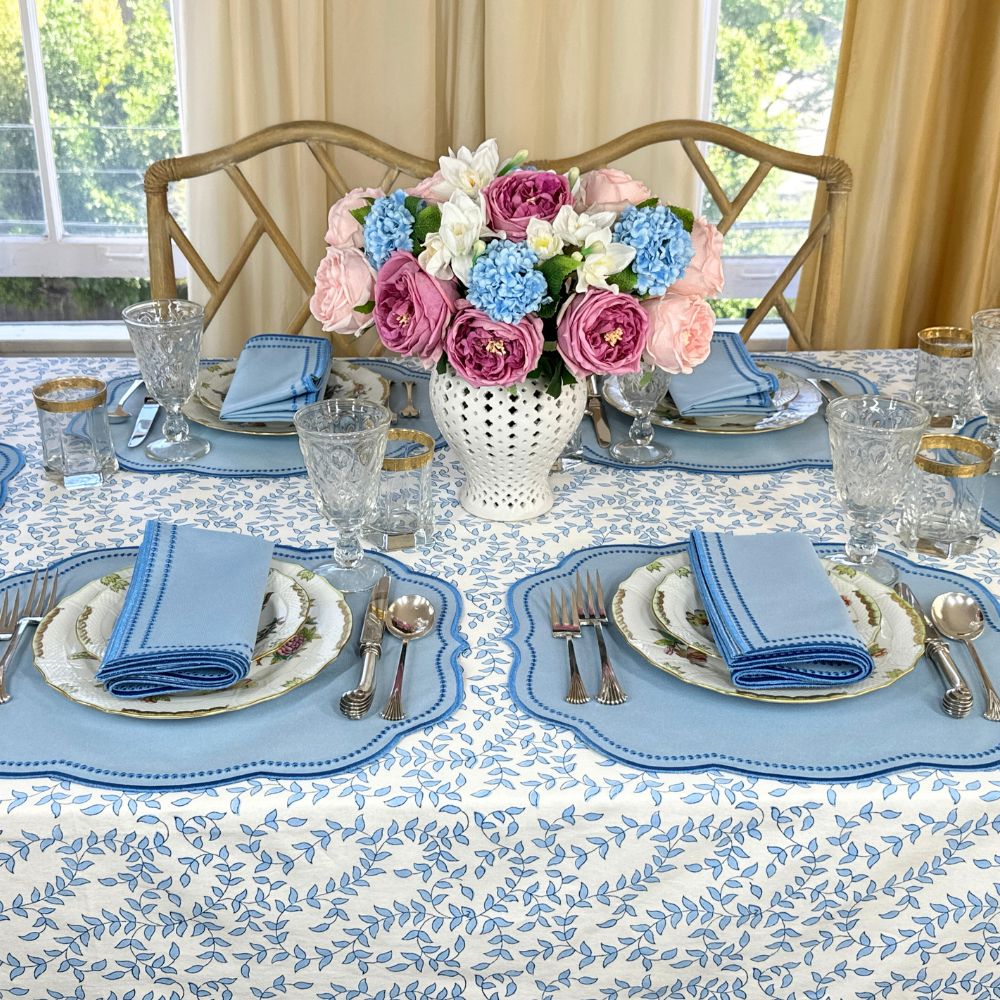Elegant table setting with floral centerpiece, blue and white tablecloth, and silverware.