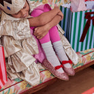Meri Meri x Marjen Sabrina pink glitter Mary Jane with red velvet bow, worn by child hugging her knees