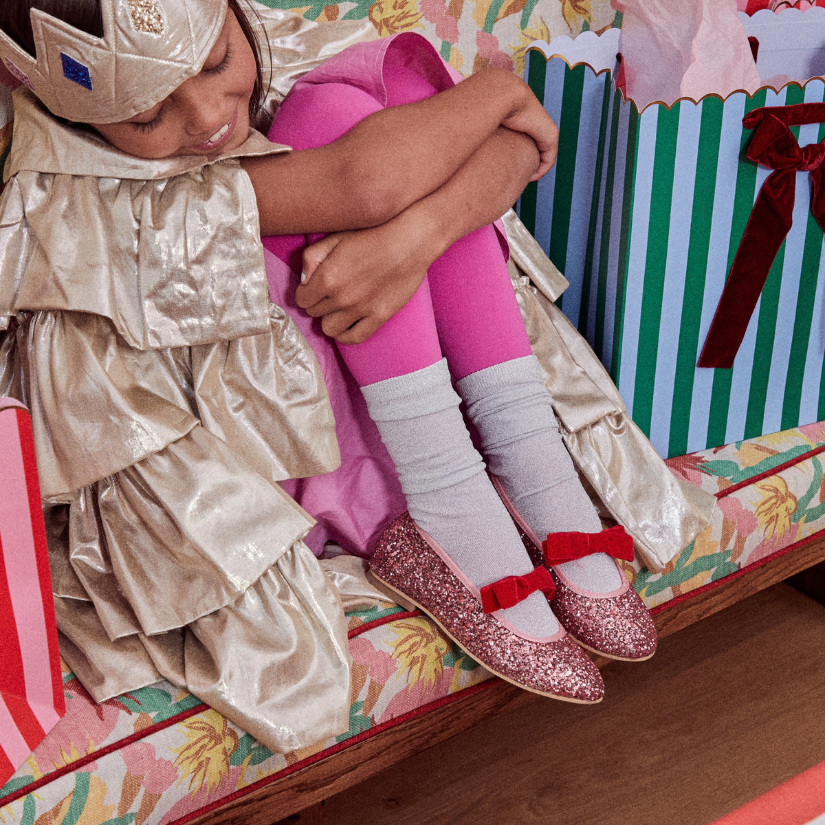 Meri Meri x Marjen Sabrina pink glitter Mary Jane with red velvet bow, worn by child hugging her knees