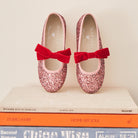 Meri Meri x Marjen Sabrina pink glitter Mary Jane with red velvet bow, pair on a stack of books
