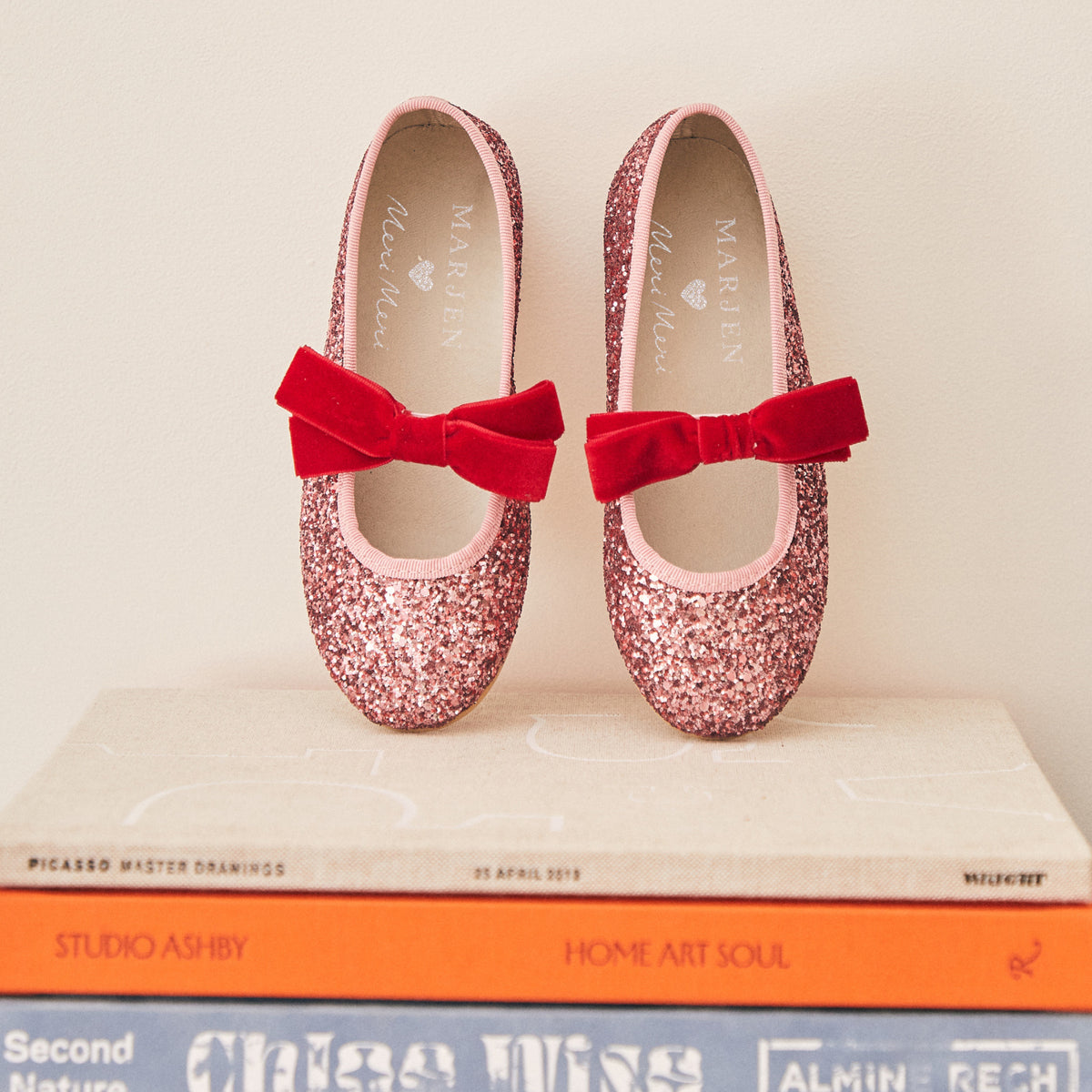 Meri Meri x Marjen Sabrina pink glitter Mary Jane with red velvet bow, pair on a stack of books