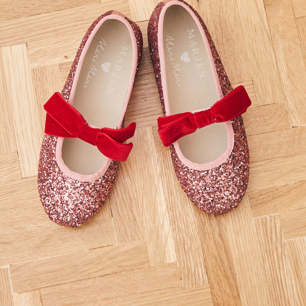 Meri Meri x Marjen Sabrina pink glitter Mary Jane with red velvet bow, pair on a parquet floor