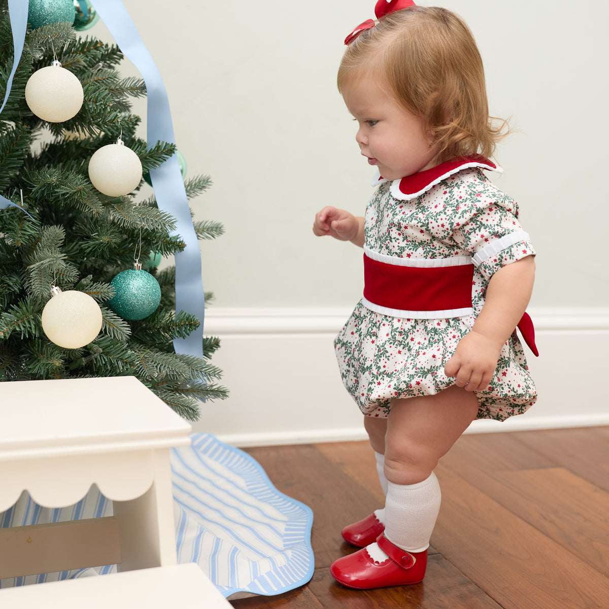Grace Bubble in Regent Wreaths holiday print with red velvet sash and Peter Pan collar, finished with crisp white pleated trim for baby and toddler girls.